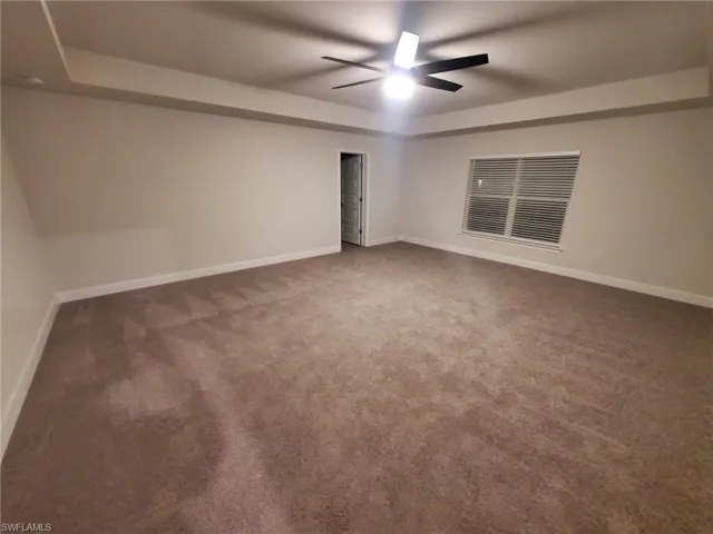Empty room featuring dark colored carpet and ceiling fan