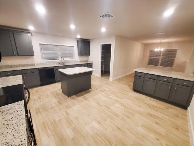 Kitchen with a center island, black appliances, sink, light stone countertops, and light hardwood / wood-style floors