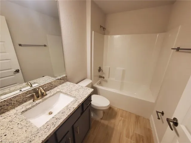 Full bathroom with vanity, hardwood / wood-style floors, washtub / shower combination, and toilet