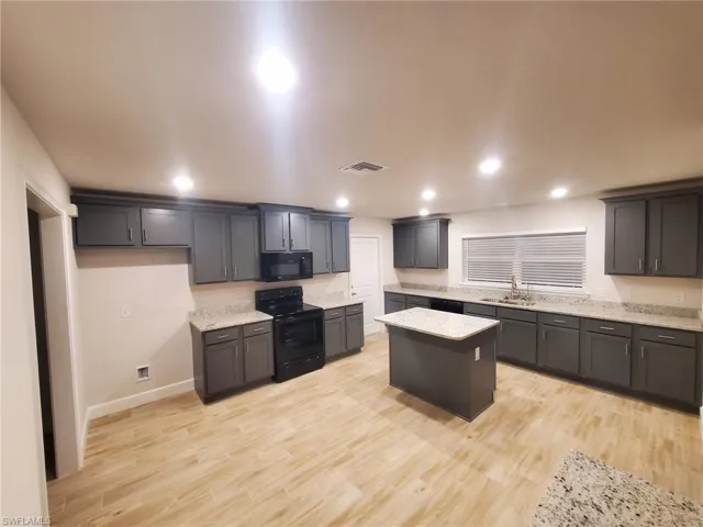 Kitchen featuring light stone counters, a center island, black appliances, and light hardwood / wood-style flooring