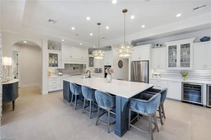 Two tone kitchen with glass fronted cabinets, decorative backsplash, a breakfast bar area, arched walkways, and ornamental molding