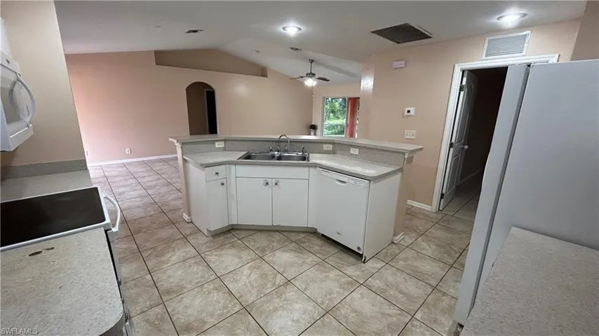 Kitchen with white cabinets, vaulted ceiling, white appliances, sink, and ceiling fan