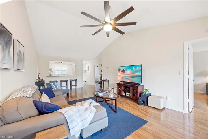 Living room featuring baseboards, light wood-style flooring, a ceiling fan, and high vaulted ceiling