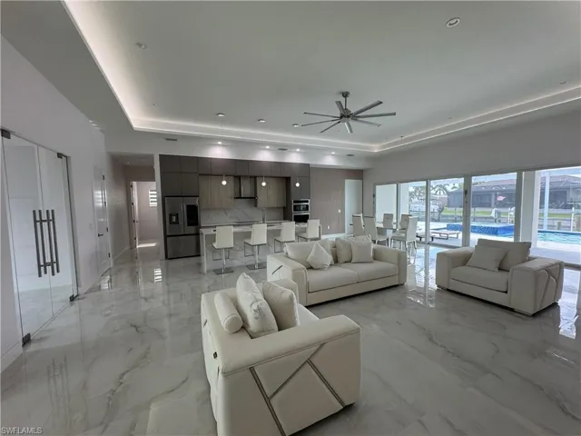 Living room featuring a raised ceiling, light marble finish floors, and ceiling fan