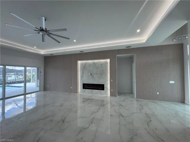 Unfurnished living room featuring ceiling fan, a fireplace, and a raised ceiling