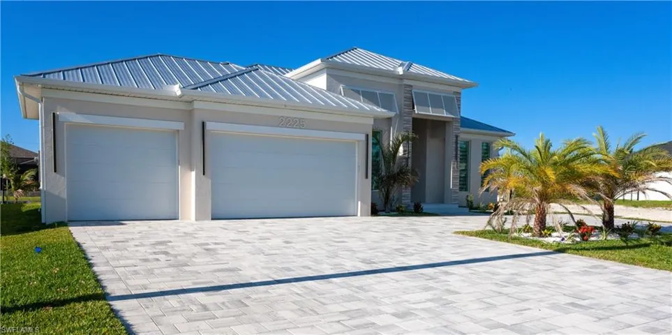 View of front of home featuring a standing seam roof, an attached garage, metal roof, stucco siding, and decorative driveway