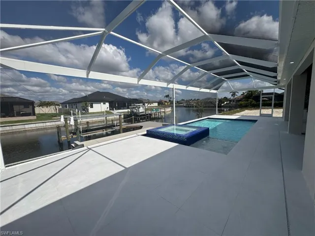 View of swimming pool with a lanai, a water view, a patio area, a boat dock, and an in ground hot tub