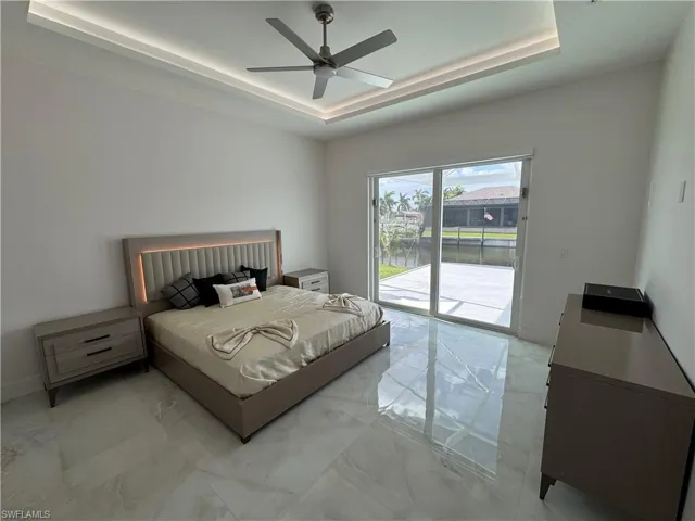 Bedroom with a raised ceiling, access to exterior, light marble finish flooring, and ceiling fan