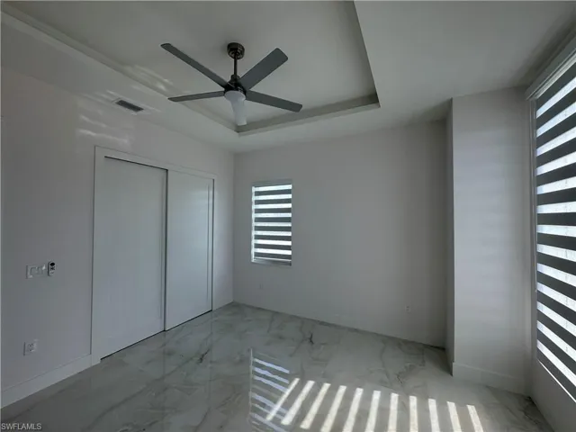 Unfurnished bedroom featuring multiple windows, a closet, a raised ceiling, and ceiling fan