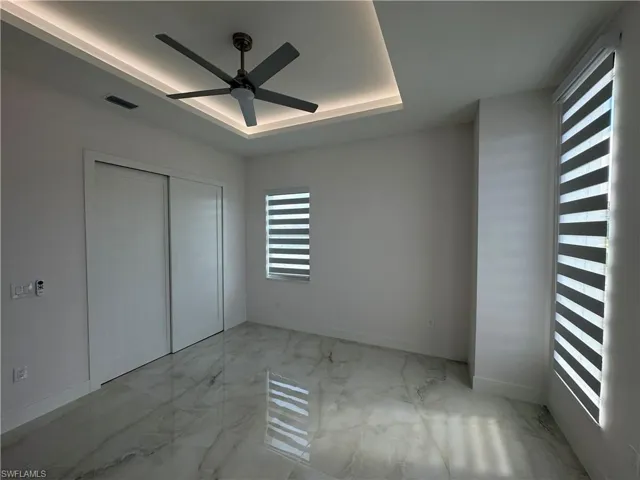 Unfurnished bedroom featuring a tray ceiling, a closet, and ceiling fan