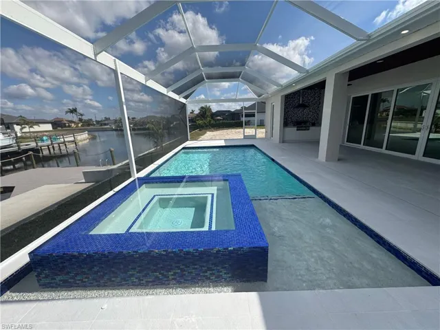 View of swimming pool featuring an in ground hot tub, a water view, glass enclosure, and a patio