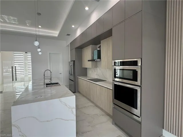 Kitchen with sink, hanging light fixtures, light stone countertops, a center island with sink, and a raised ceiling