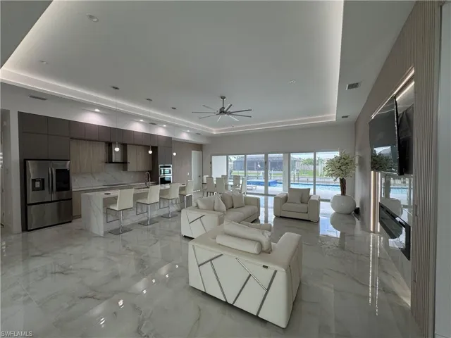 Living room featuring a tray ceiling, light marble finish flooring, a ceiling fan, and recessed lighting