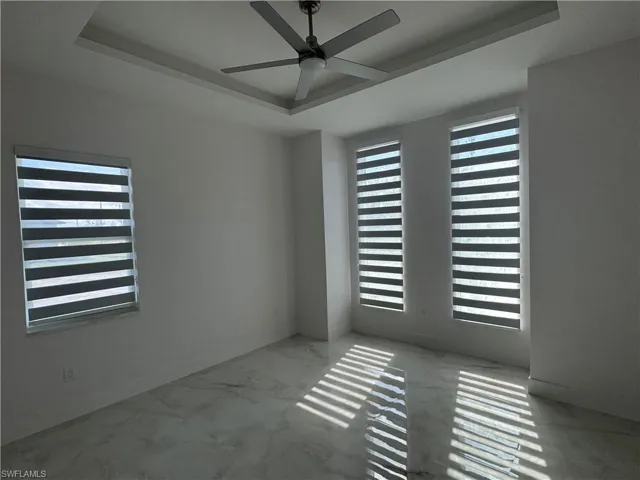 Spare room with ceiling fan, plenty of natural light, and a tray ceiling