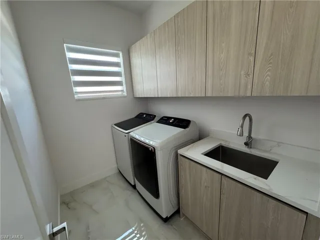 Washroom featuring cabinet space, washer and clothes dryer, and light marble finish floors