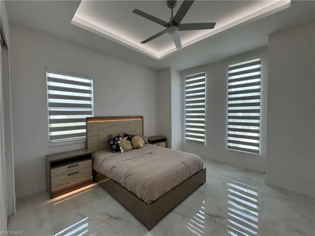Bedroom with a raised ceiling, multiple windows, marble finish floors, and ceiling fan