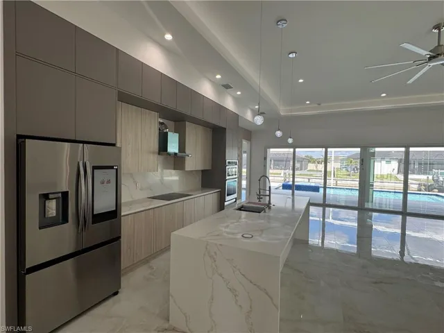 Kitchen with sink, decorative light fixtures, a center island with sink, stainless steel appliances, and light stone countertops