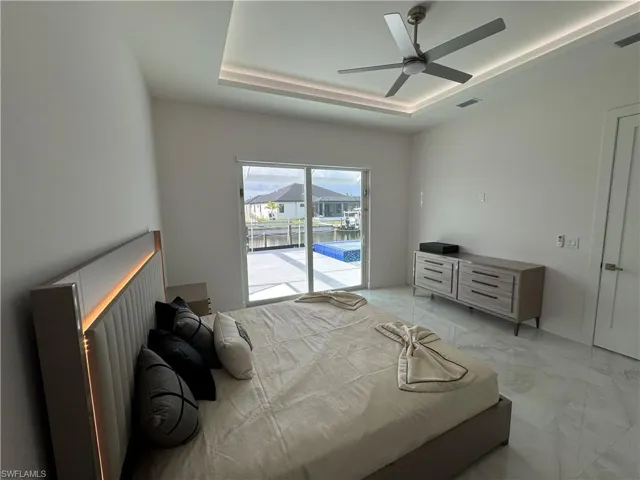 Bedroom featuring access to exterior, a tray ceiling, light marble finish floors, and a ceiling fan