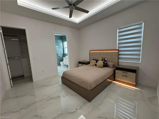 Bedroom with marble finish floors, a spacious closet, a raised ceiling, and a closet