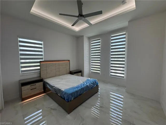 Bedroom with a raised ceiling, marble look tile flooring, and a ceiling fan