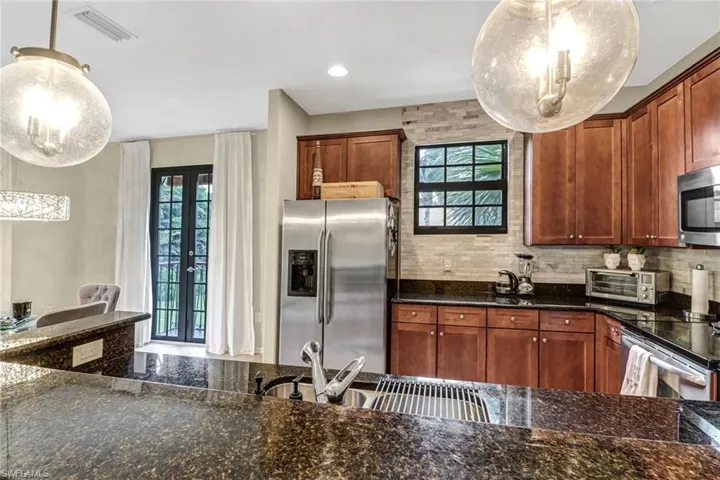 Kitchen featuring decorative light fixtures, french doors, dark stone counters, and appliances with stainless steel finishes