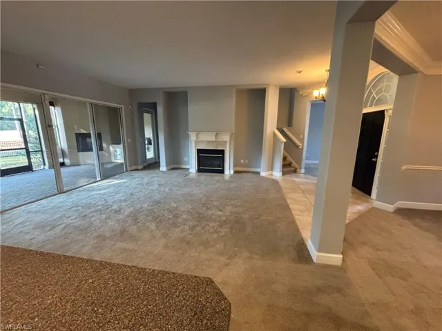 Unfurnished living room with carpet flooring, a fireplace with flush hearth, a chandelier, crown molding, and stairs