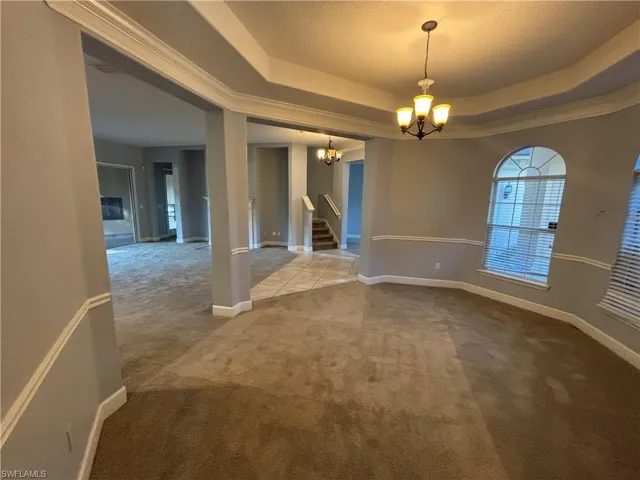 Unfurnished room featuring carpet floors, stairway, a chandelier, a raised ceiling, and a textured ceiling