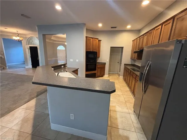 Kitchen featuring black appliances, dark countertops, brown cabinetry, recessed lighting, and light tile patterned floors
