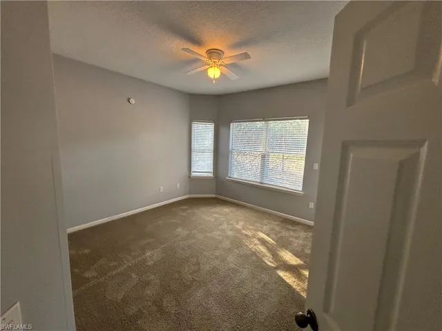 Empty room with a textured ceiling, dark carpet, and a ceiling fan