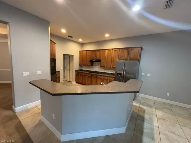 Kitchen with dark countertops, brown cabinetry, black appliances, decorative backsplash, and recessed lighting