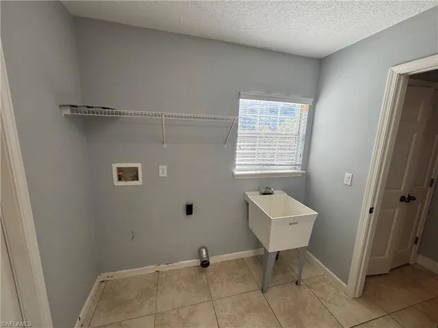 Washroom with a textured ceiling, washer hookup, and light tile patterned floors