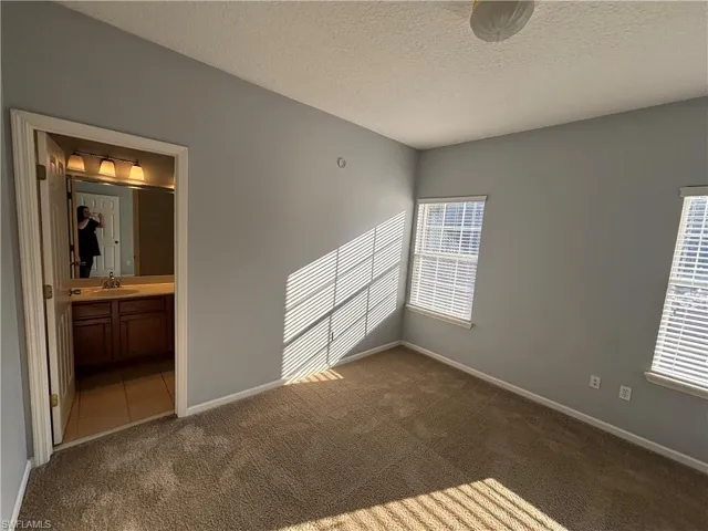 Unfurnished bedroom with a textured ceiling, dark colored carpet, and ensuite bathroom
