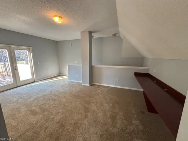Bonus room featuring a textured ceiling, carpet floors, french doors, and lofted ceiling