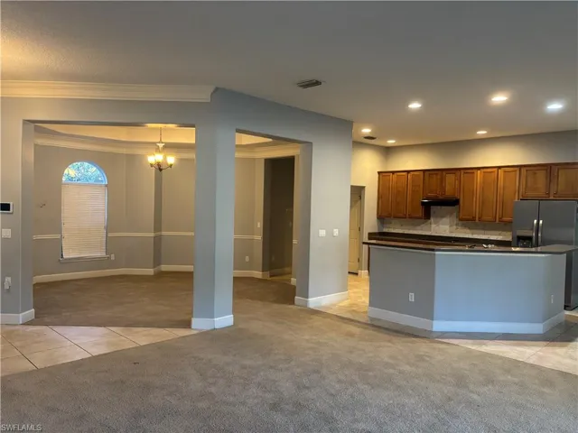 Kitchen featuring light tile patterned flooring, dark countertops, decorative backsplash, brown cabinetry, and stainless steel fridge