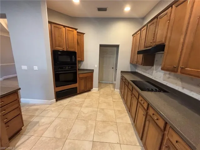 Kitchen featuring brown cabinets, black appliances, recessed lighting, under cabinet range hood, and a warming drawer