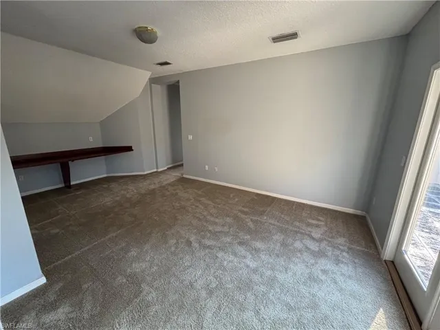 Additional living space with a textured ceiling, dark colored carpet, and lofted ceiling
