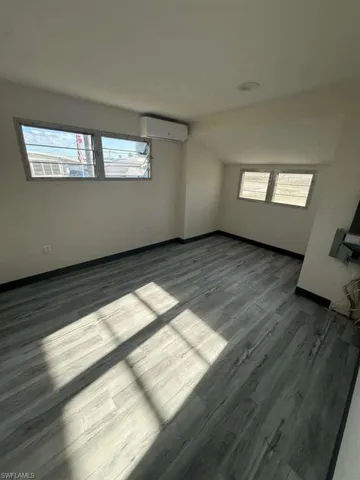 Empty room featuring healthy amount of natural light, wood finished floors, and a wall unit AC