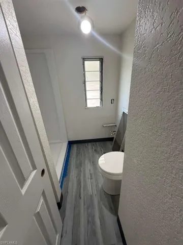 Full bathroom with wood finished floors, a textured wall, and a stall shower