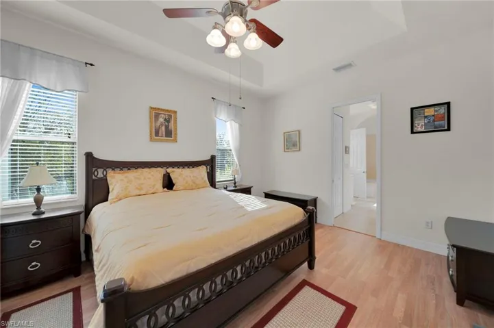Bedroom featuring visible vents, ceiling fan, baseboards, light wood-style floors, and a raised ceiling
