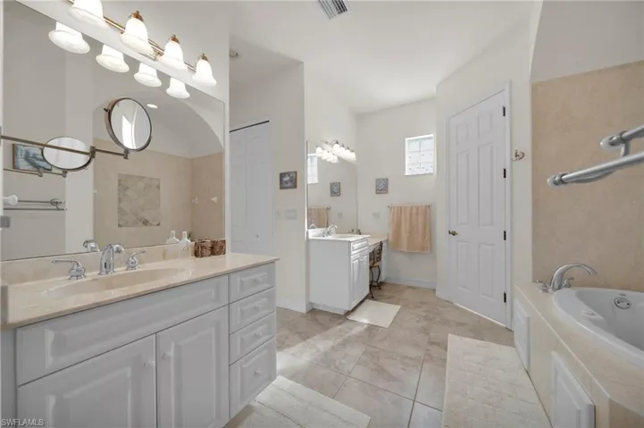 Bathroom with a garden tub, two vanities, visible vents, and a sink