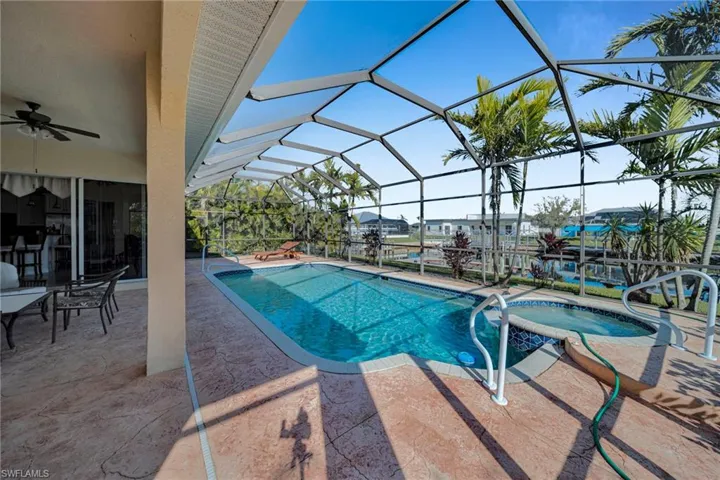 View of swimming pool with a patio area, glass enclosure, a pool with connected hot tub, and a ceiling fan