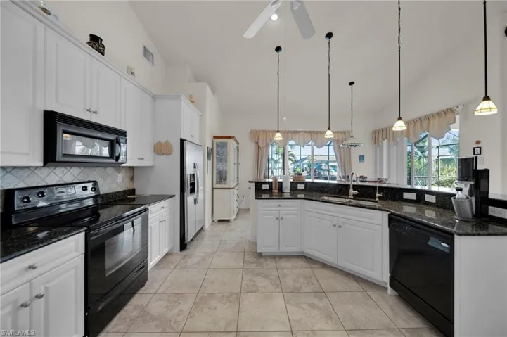 Kitchen featuring tasteful backsplash, white cabinetry, black appliances, and a sink