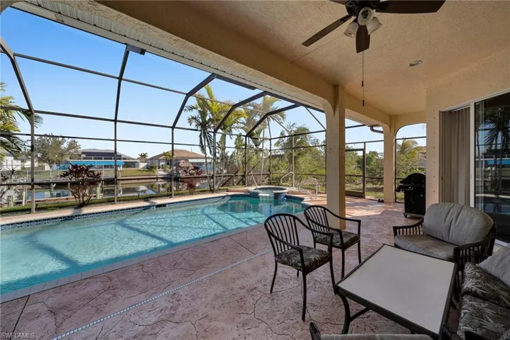 View of pool featuring a pool with connected hot tub, ceiling fan, glass enclosure, a grill, and a patio