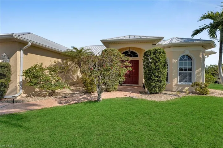 View of front of house featuring stucco siding, metal roof, and a front yard