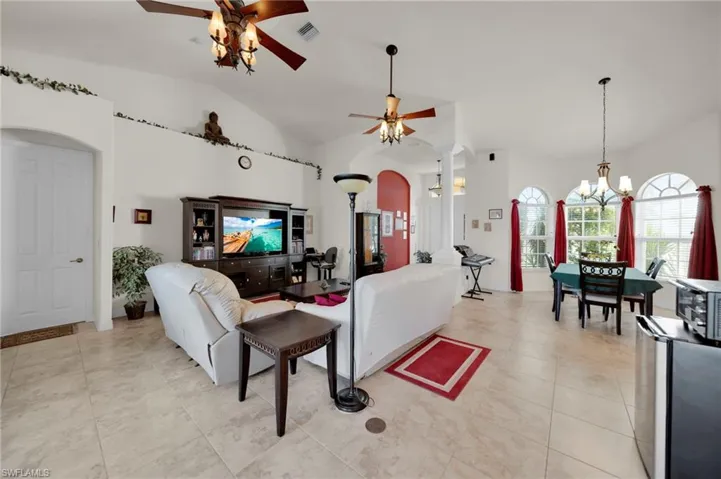 Living area with visible vents, lofted ceiling, decorative columns, ceiling fan with notable chandelier, and light tile patterned flooring