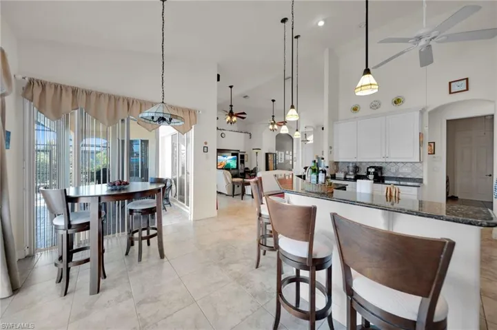 Kitchen featuring a ceiling fan, high vaulted ceiling, arched walkways, white cabinets, and backsplash