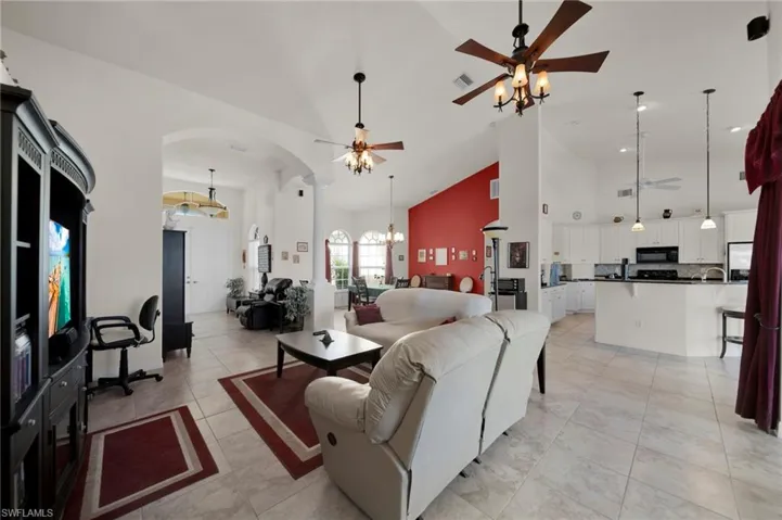 Living area with light tile patterned flooring, ceiling fan with notable chandelier, arched walkways, and high vaulted ceiling