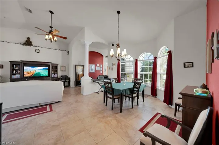 Dining space featuring visible vents, high vaulted ceiling, decorative columns, arched walkways, and ceiling fan with notable chandelier