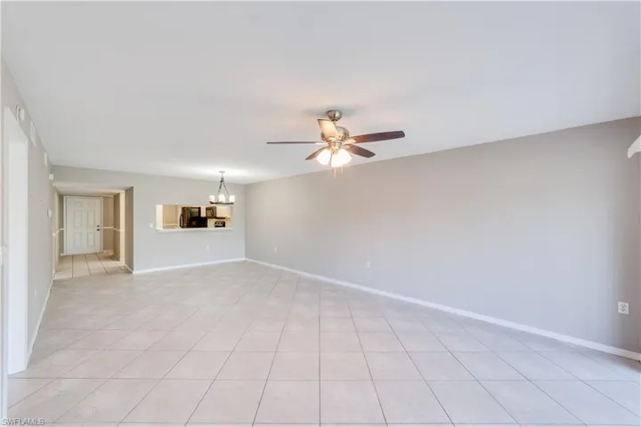 Unfurnished living room featuring light tile flooring and ceiling fan with notable chandelier