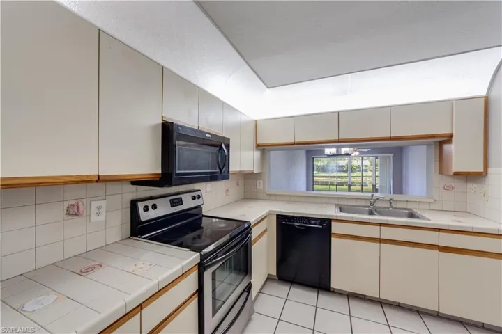 Kitchen featuring tile counters, black appliances, backsplash, light tile floors, and sink